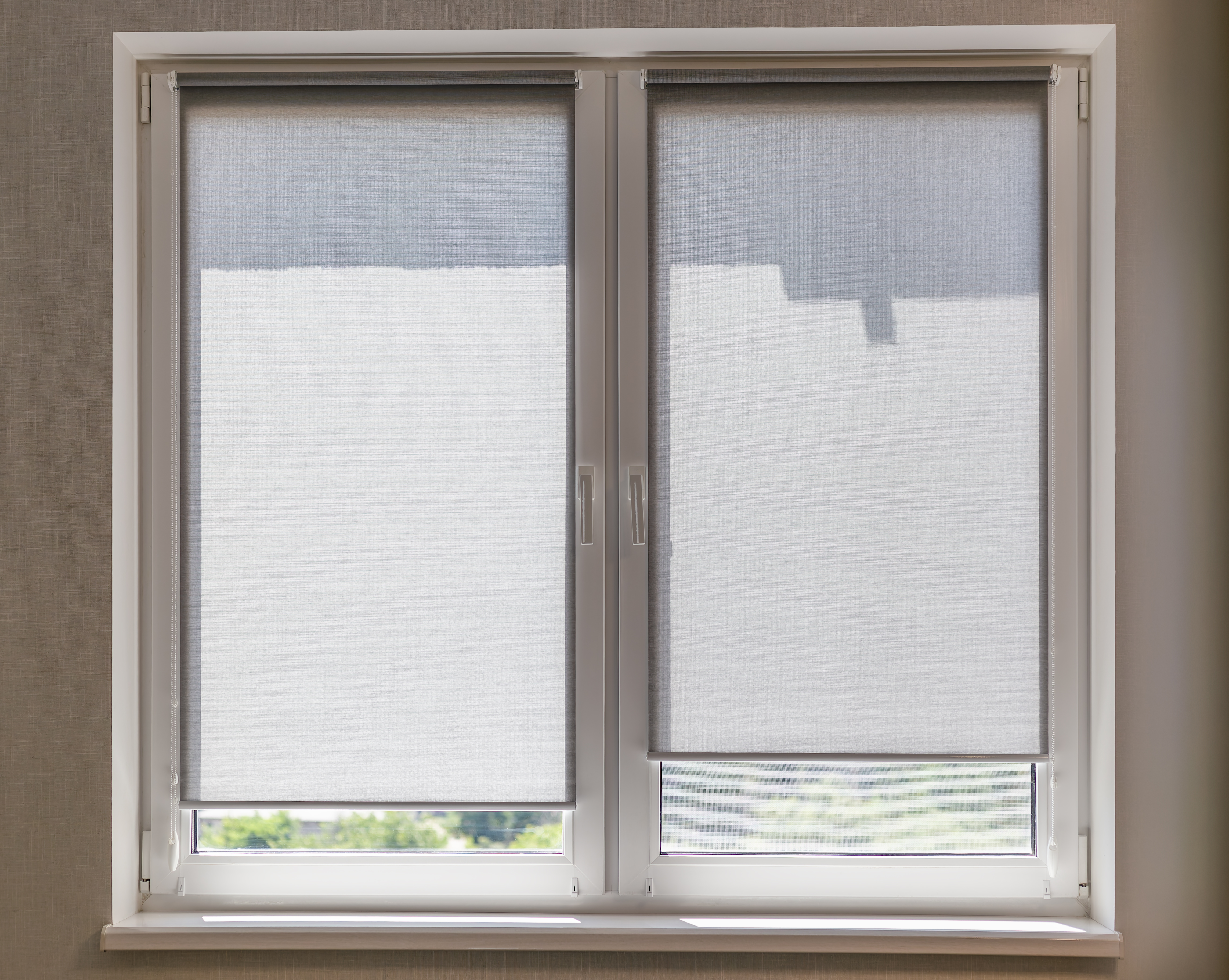 Gray roller blinds on the window close-up in the room on a sunny day. Small roller shades on the window sashes. Sunshade textured fabric with darkening ability.